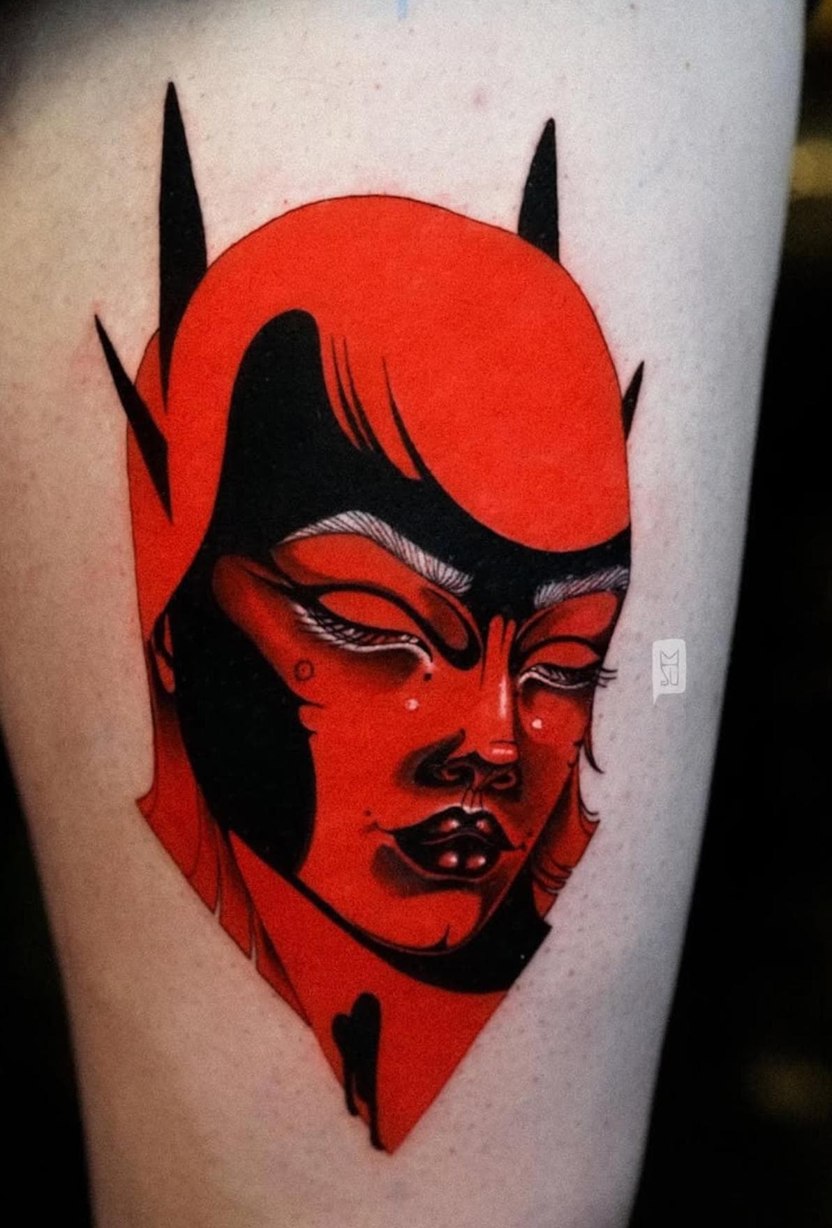 Red and black illustrative devil face tattoo on thigh