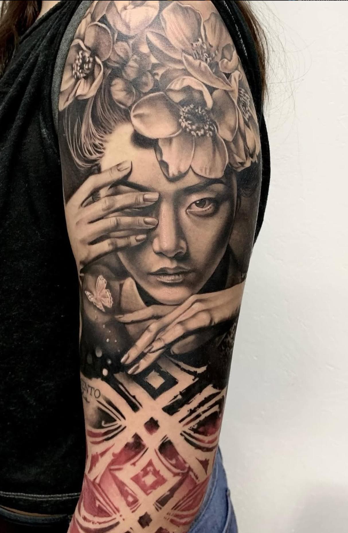Black and grey realistic portrait with floral elements and red geometric Trash Polka patterns on full arm sleeve.