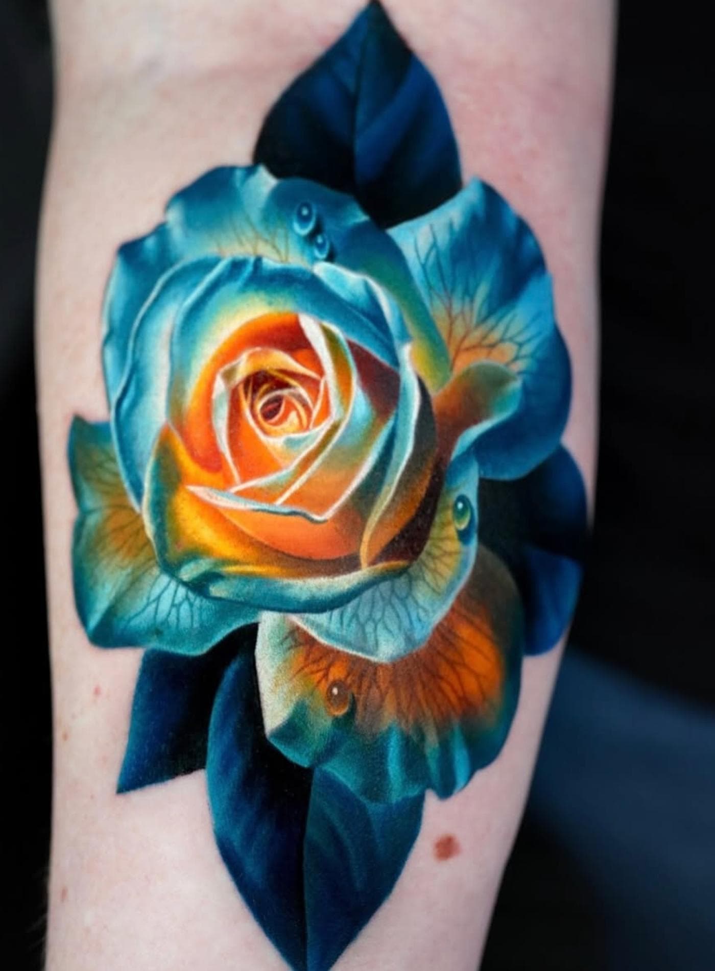 Vibrant and realistic rose tattoo on the forearm with blue and orange hues.