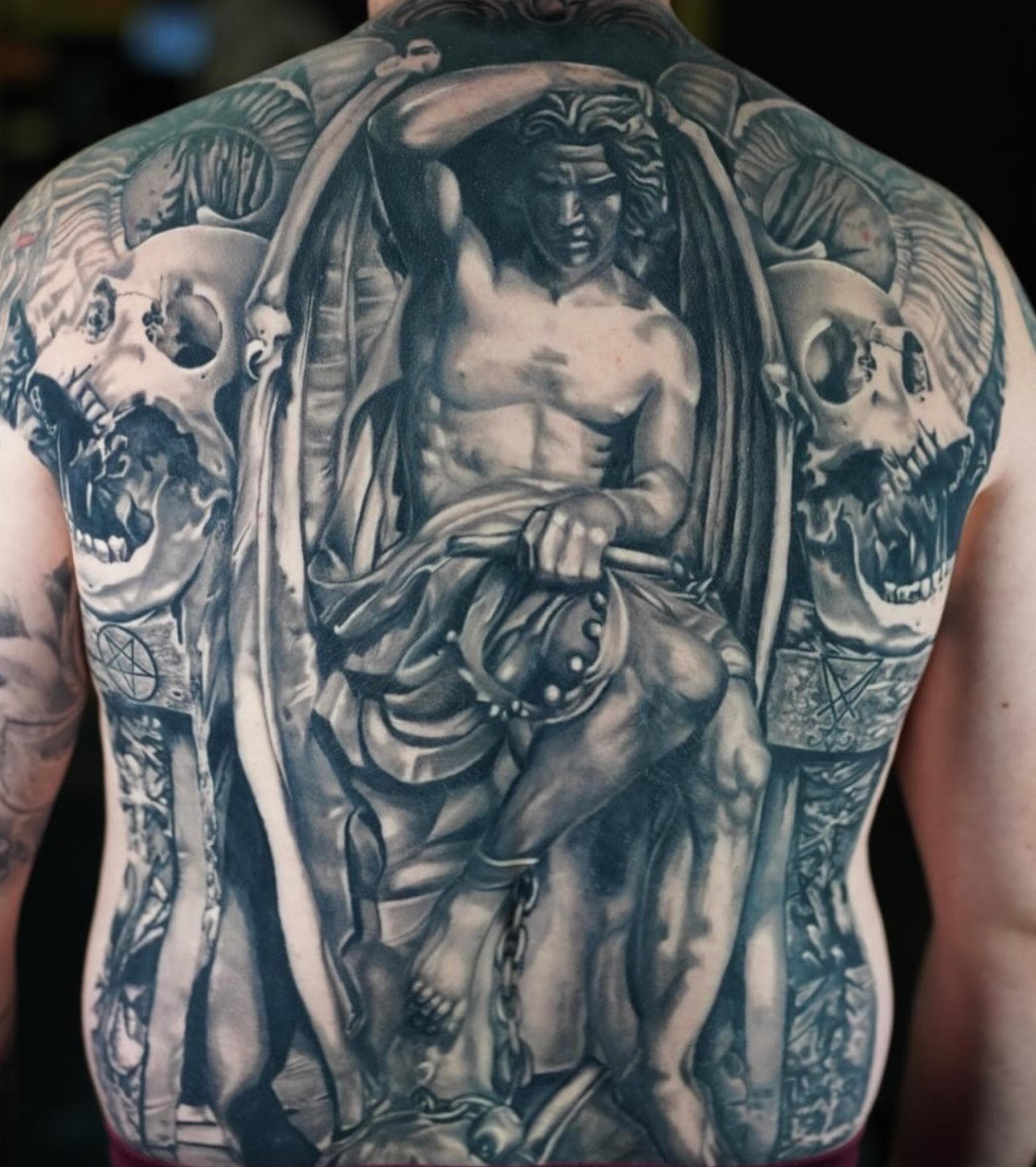 Black and grey realism tattoo of an archangel and skulls on full back
